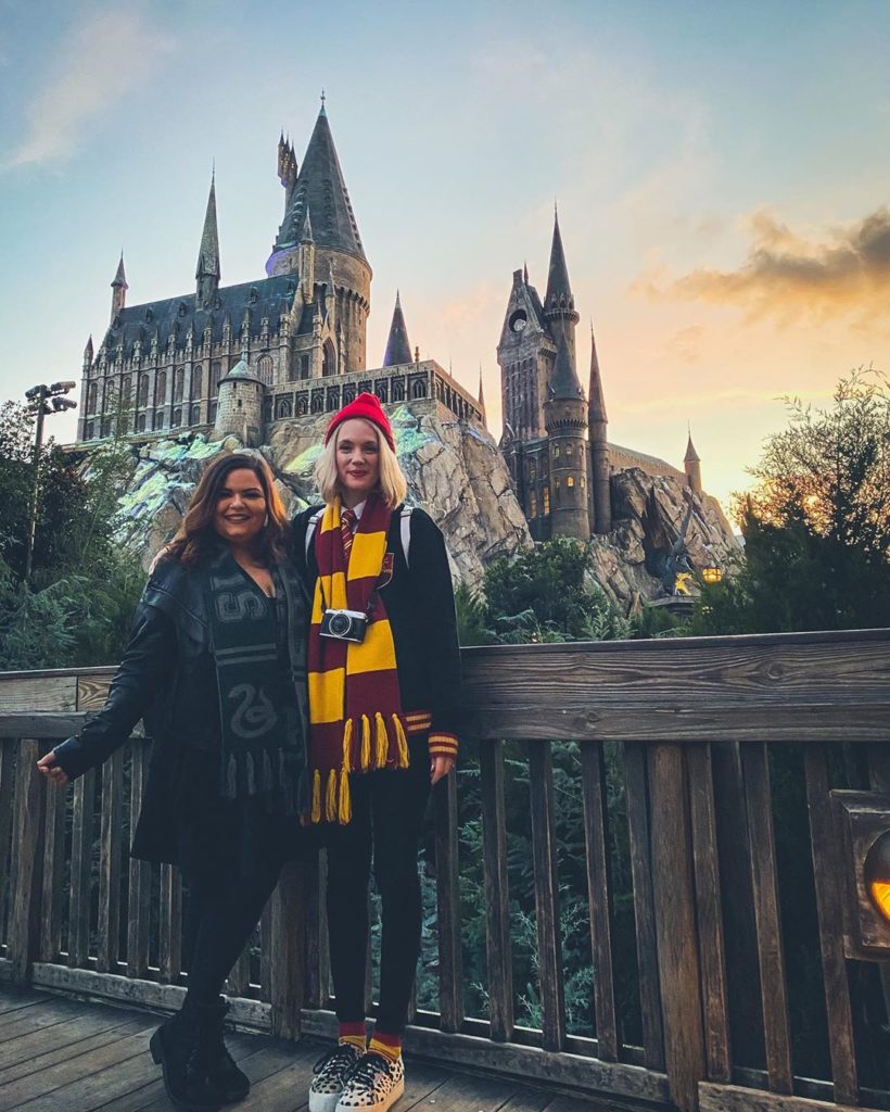 Two girls posing in Hogwarts house attire in front of Hogwarts castle
